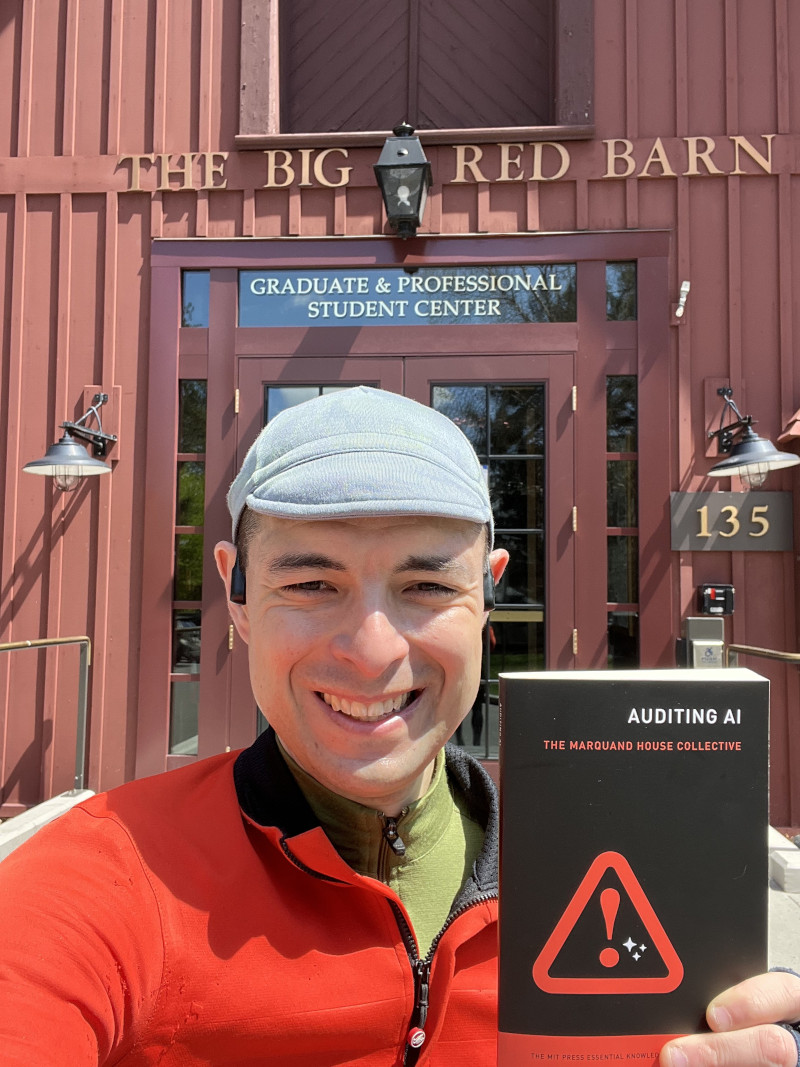 Image of J. Nathan Matias holding the book 'Auditing AI' in front of the Cornell University Big Red Barn