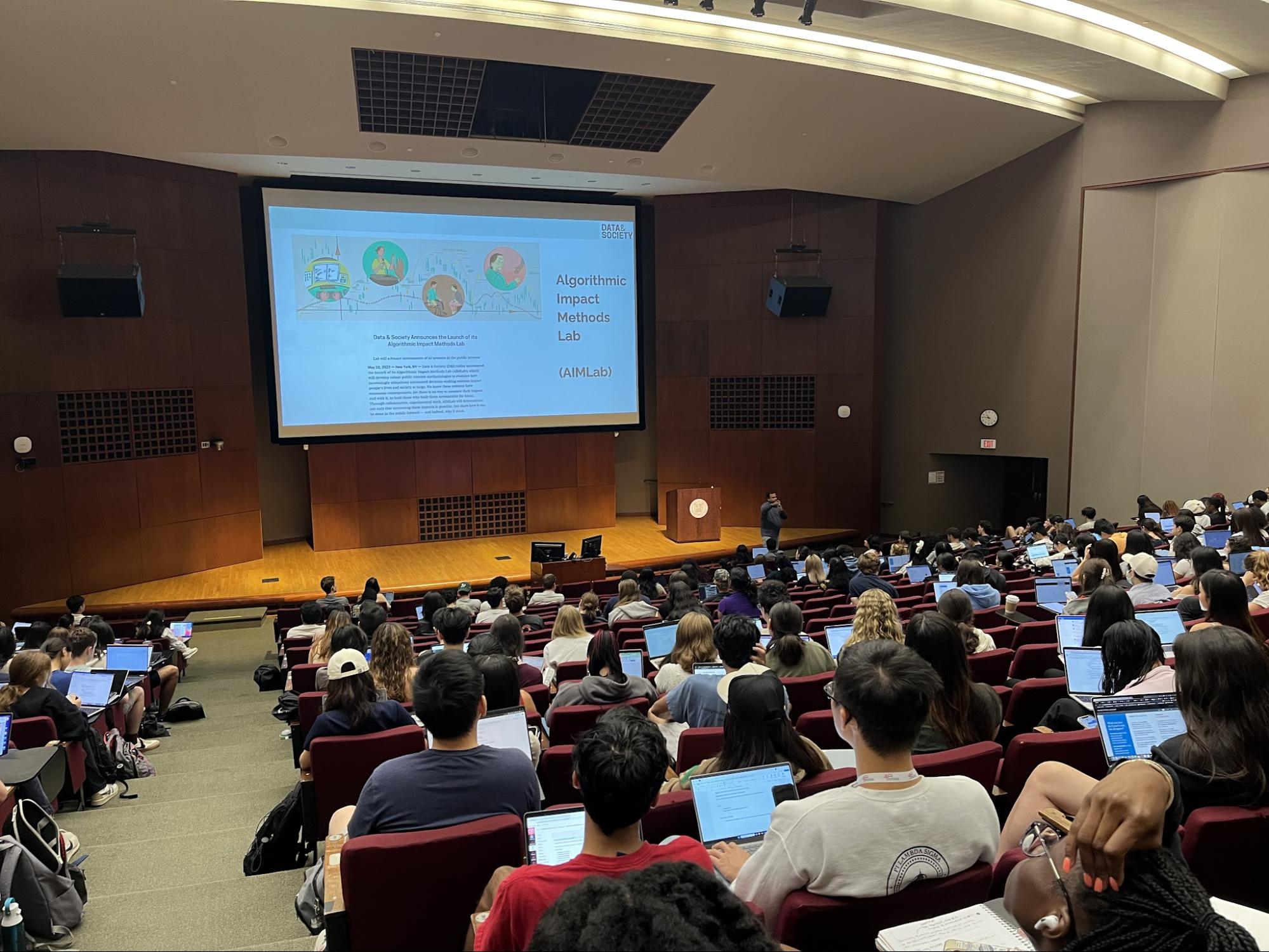 A lecturer speaks to a large room of students